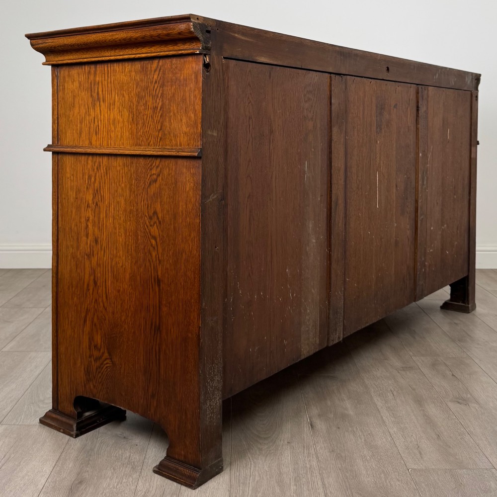 An early 20th-century oak Arts and Crafts sideboard featuring hand-carved foliate panels, copper drop handles, multiple drawers, and a central open recess. View V