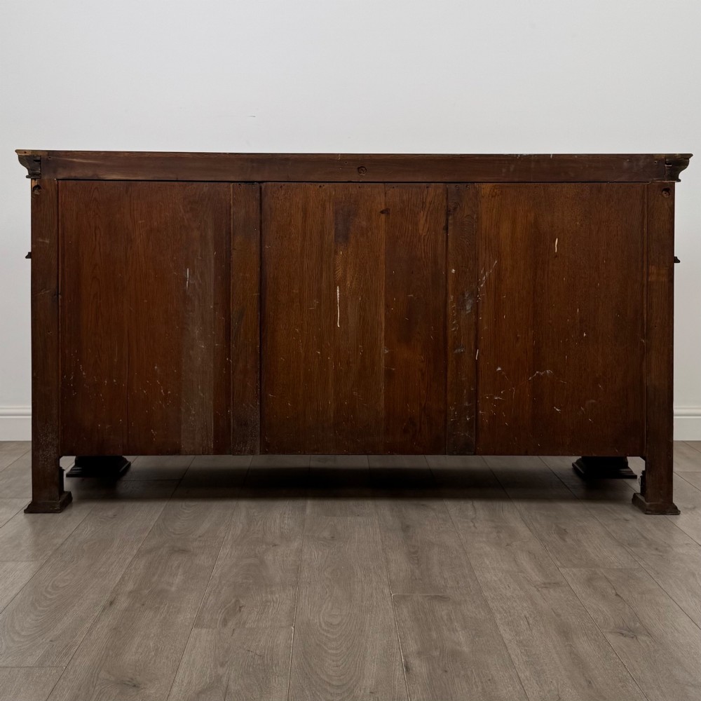 An early 20th-century oak Arts and Crafts sideboard featuring hand-carved foliate panels, copper drop handles, multiple drawers, and a central open recess. View VI