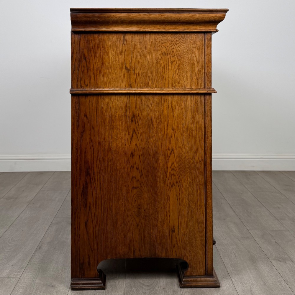 An early 20th-century oak Arts and Crafts sideboard featuring hand-carved foliate panels, copper drop handles, multiple drawers, and a central open recess. View VIII