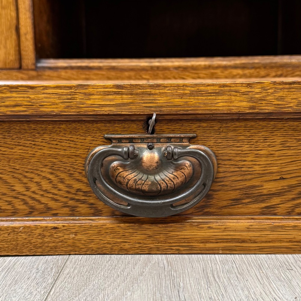 An early 20th-century oak Arts and Crafts sideboard featuring hand-carved foliate panels, copper drop handles, multiple drawers, and a central open recess. View XII