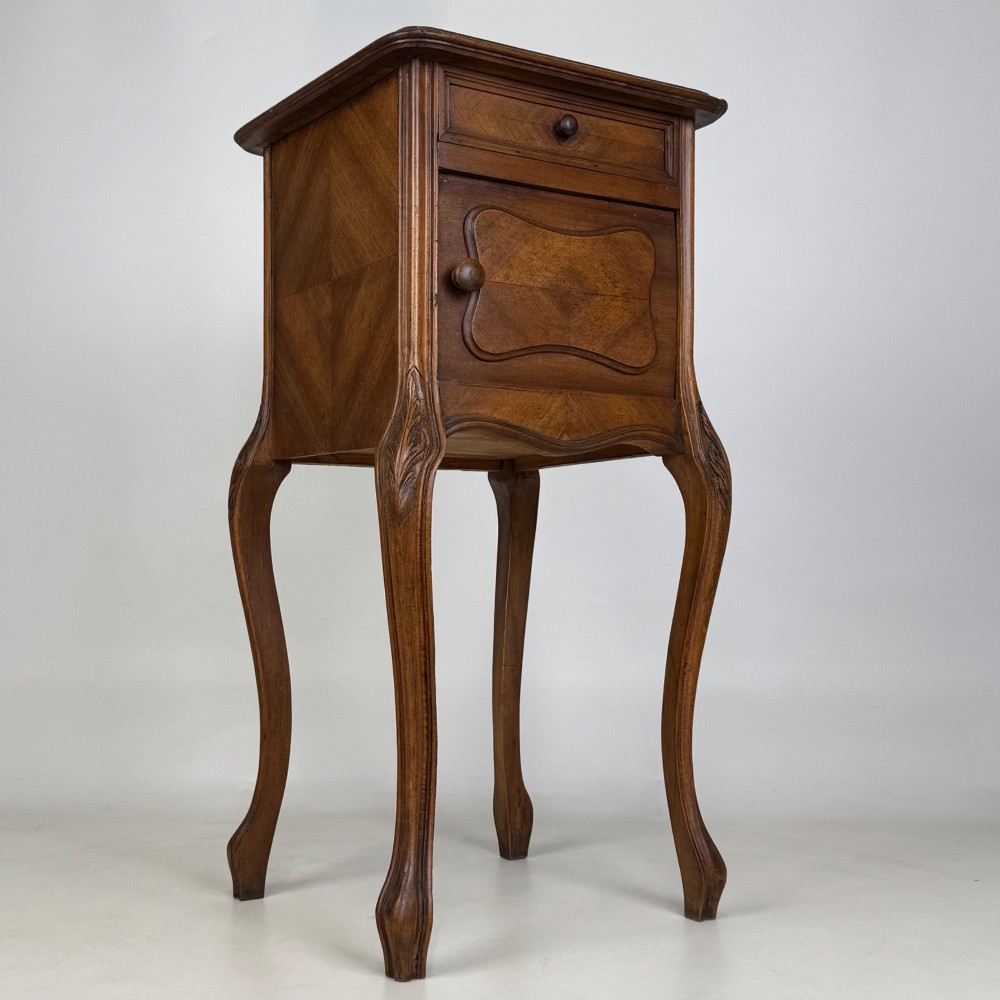 An antique French walnut bedside cabinet featuring high slender cabriole legs, a single drawer, and a carved wooden door with a marquetry panel. View IX
