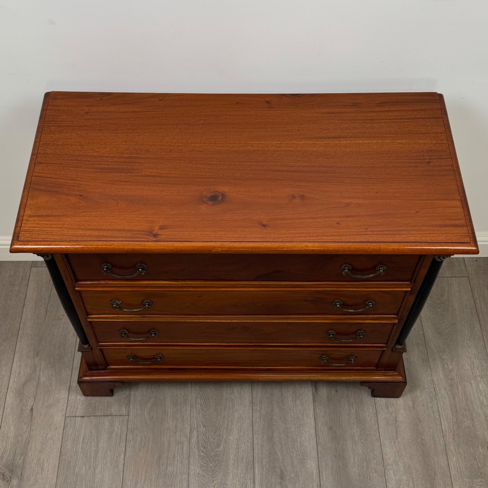 A 20th-century Georgian style mahogany chest featuring four full-width drawers with brass drop handles, flanked by ebonised side columns, resting on bracket feet. View IX