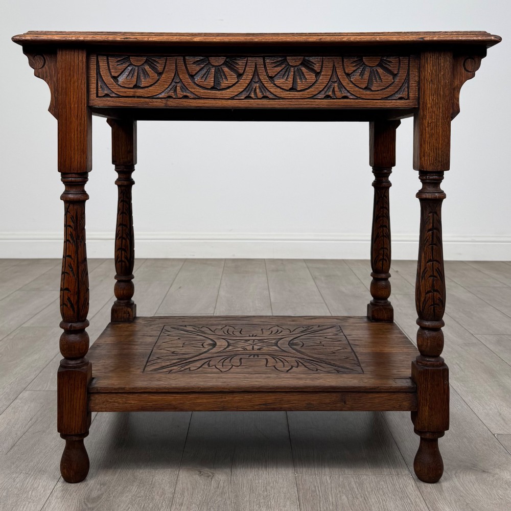 An antique Edwardian carved oak side table featuring a carved apron, four turned legs, and a carved foliate motif on its lower shelf. View V