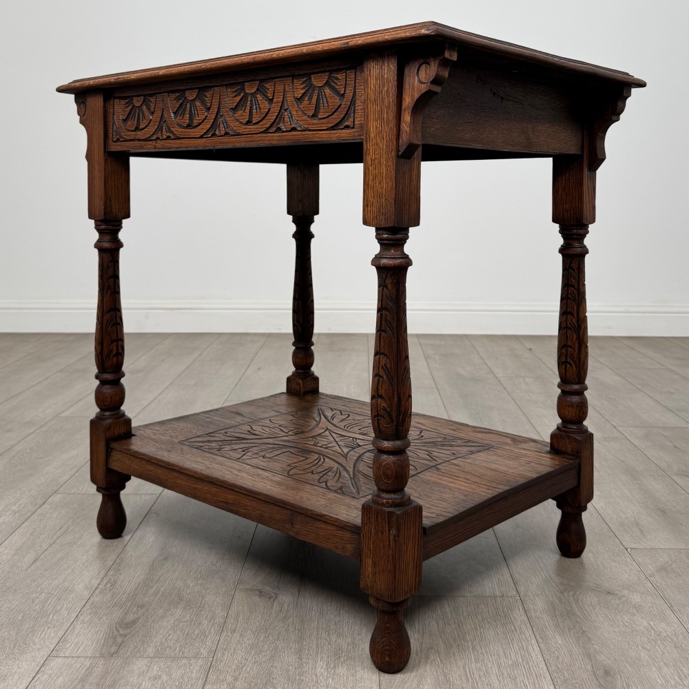 An antique Edwardian carved oak side table featuring a carved apron, four turned legs, and a carved foliate motif on its lower shelf. View VI
