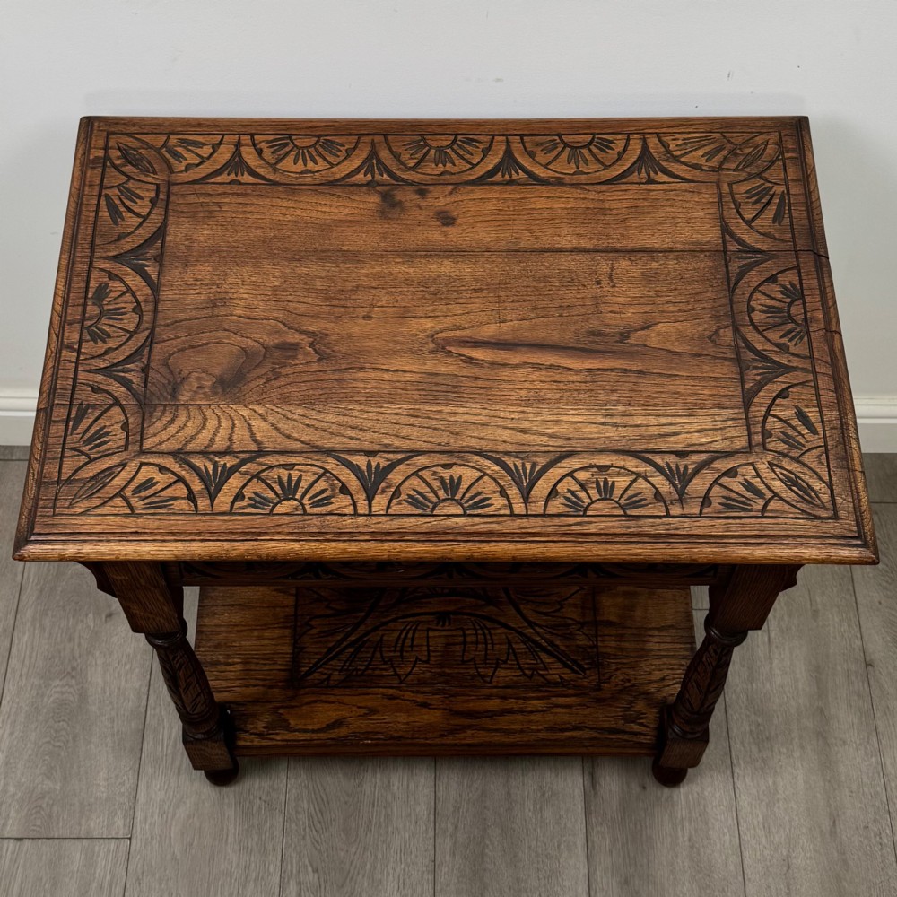 An antique Edwardian carved oak side table featuring a carved apron, four turned legs, and a carved foliate motif on its lower shelf. View IX