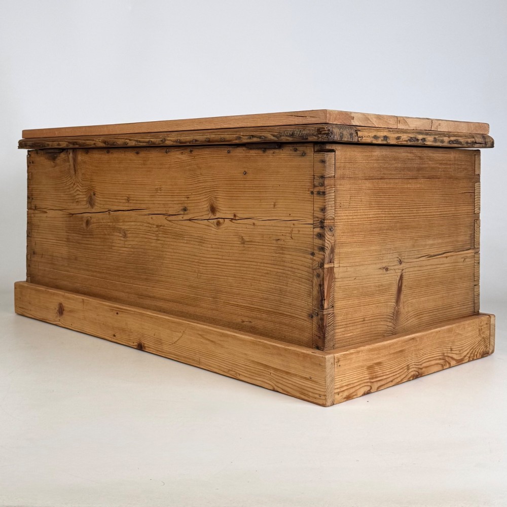 A nineteenth-century Victorian pine blanket box featuring a flat hinged lid, central iron keyhole escutcheon, visible corner joinery, and a solid plinth base. View VI