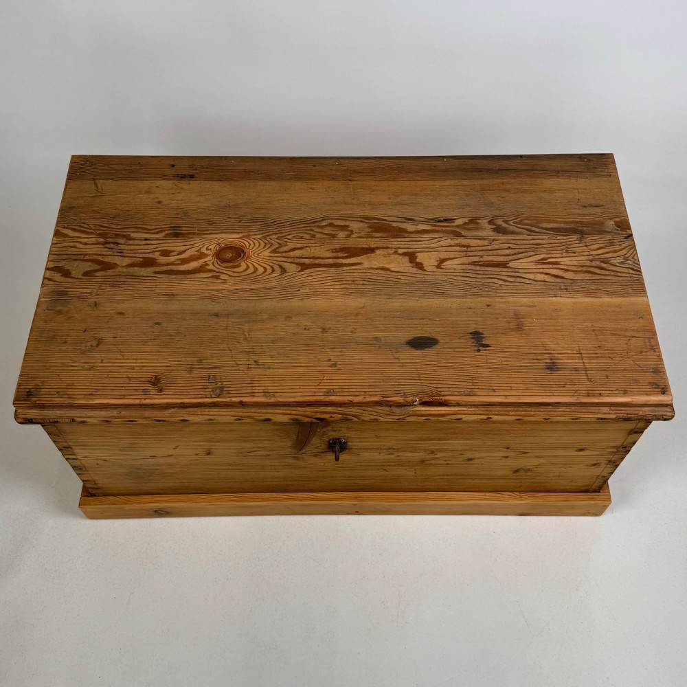 A nineteenth-century Victorian pine blanket box featuring a flat hinged lid, central iron keyhole escutcheon, visible corner joinery, and a solid plinth base. View IX