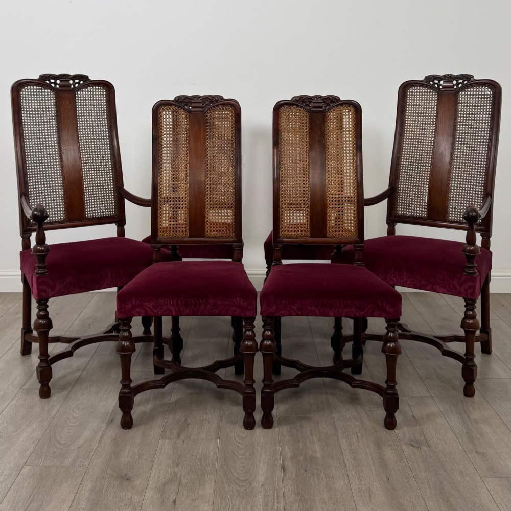 A set of mahogany dining chairs featuring high cane-panelled backs, carved top crests, turned legs, and deep red velvet seats.