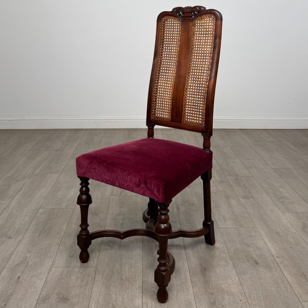A set of mahogany dining chairs featuring high cane-panelled backs, carved top crests, turned legs, and deep red velvet seats. View III