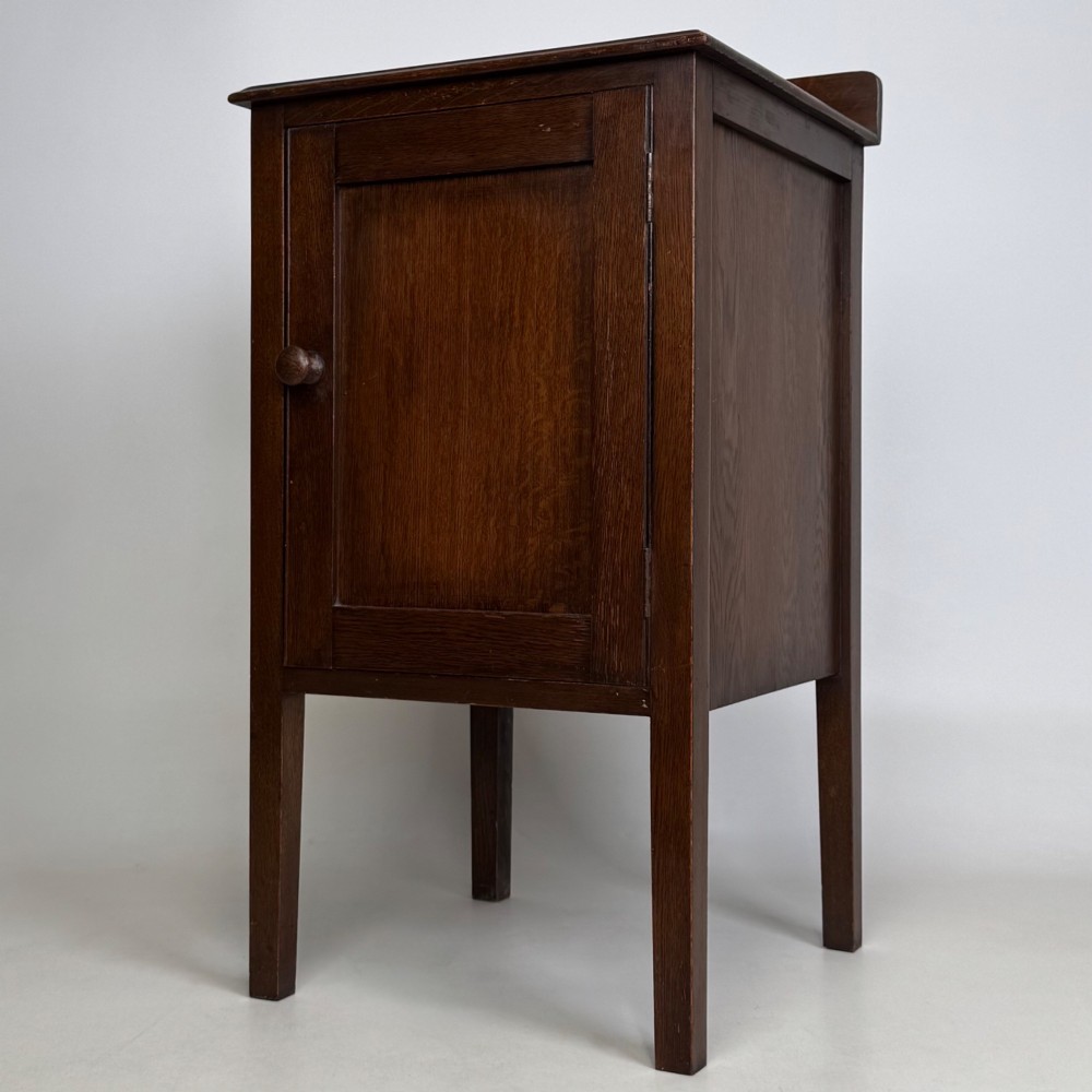 An Edwardian dark brown oak cabinet featuring a single panelled door with a round wooden knob supported on four square straight legs. View III