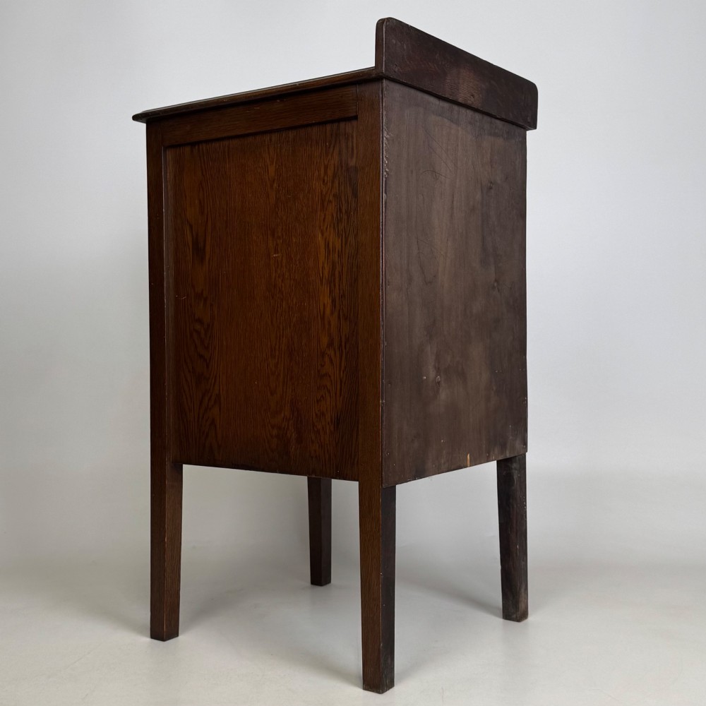 An Edwardian dark brown oak cabinet featuring a single panelled door with a round wooden knob supported on four square straight legs. View V