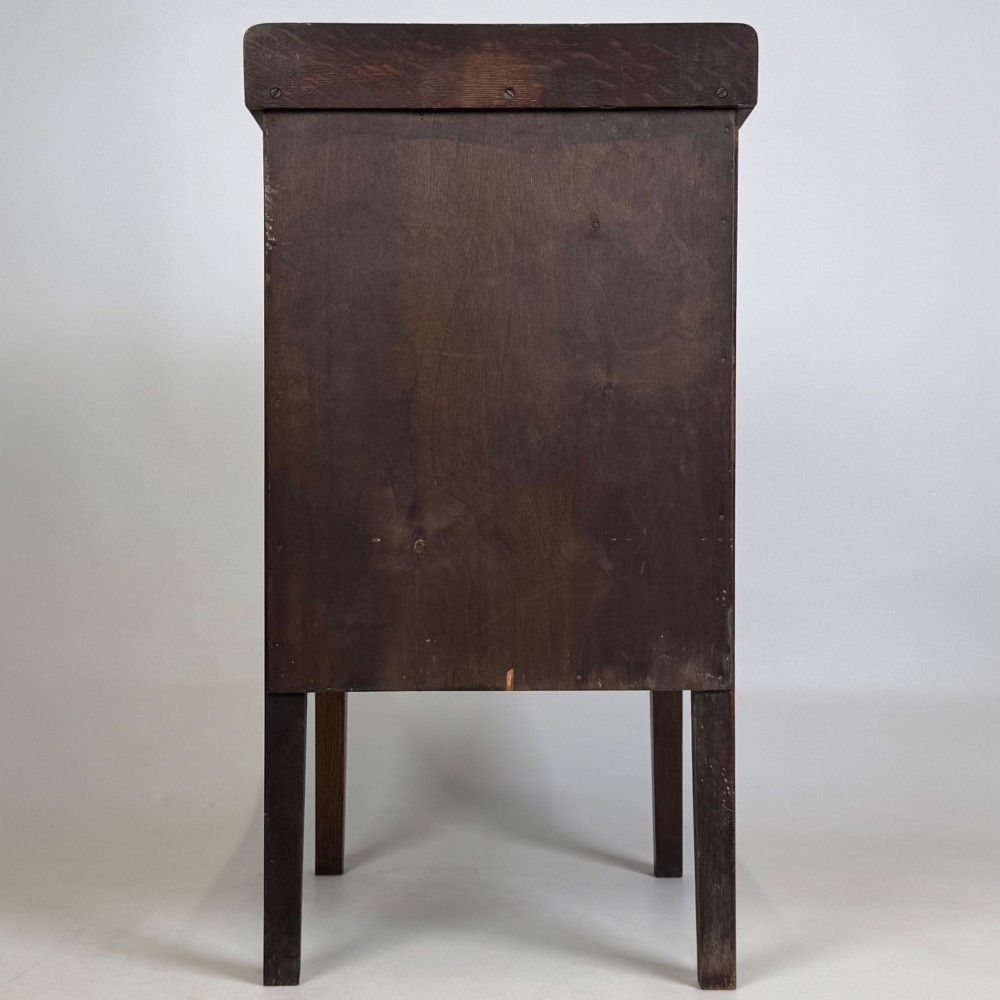 An Edwardian dark brown oak cabinet featuring a single panelled door with a round wooden knob supported on four square straight legs. View VI