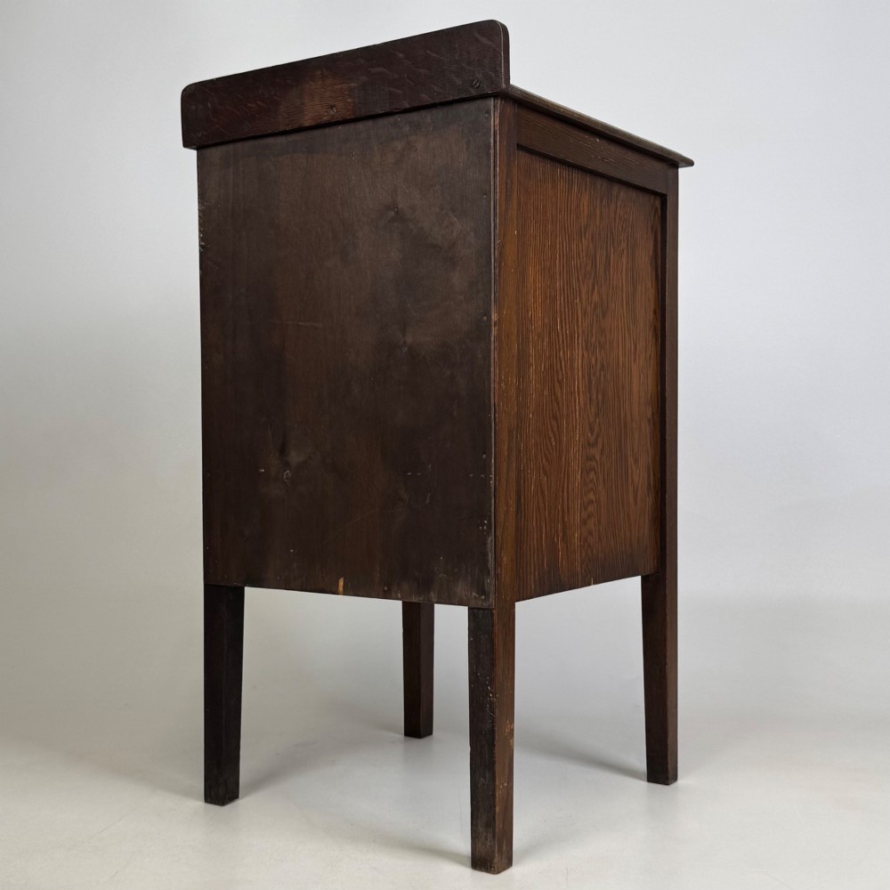 An Edwardian dark brown oak cabinet featuring a single panelled door with a round wooden knob supported on four square straight legs. View VII