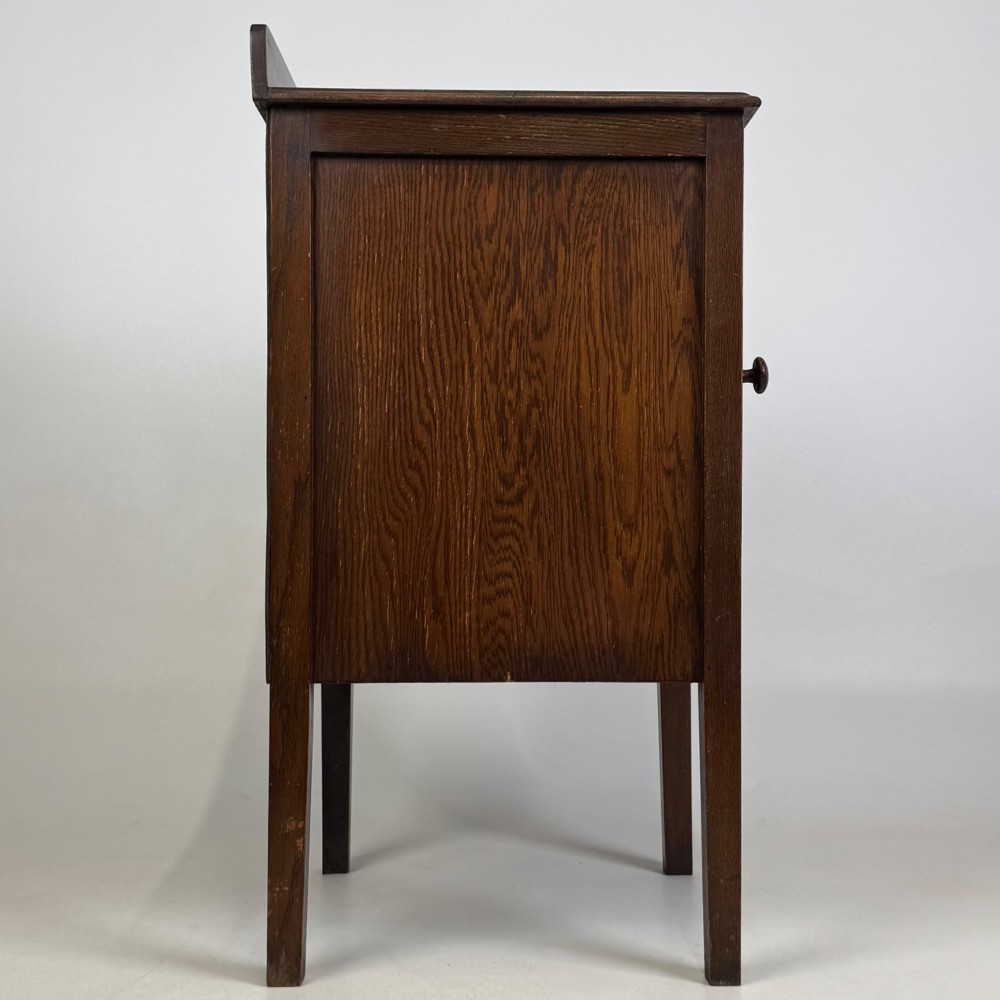 An Edwardian dark brown oak cabinet featuring a single panelled door with a round wooden knob supported on four square straight legs. View VIII