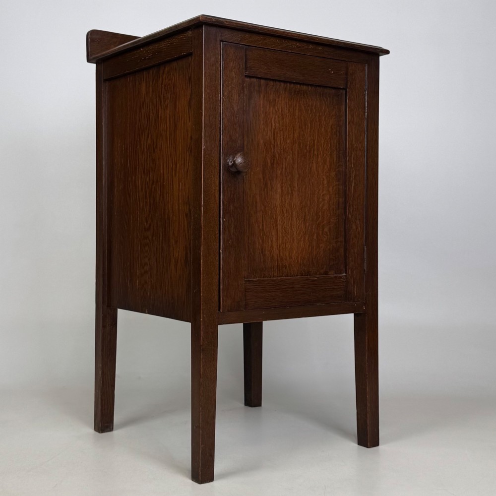An Edwardian dark brown oak cabinet featuring a single panelled door with a round wooden knob supported on four square straight legs. View IX