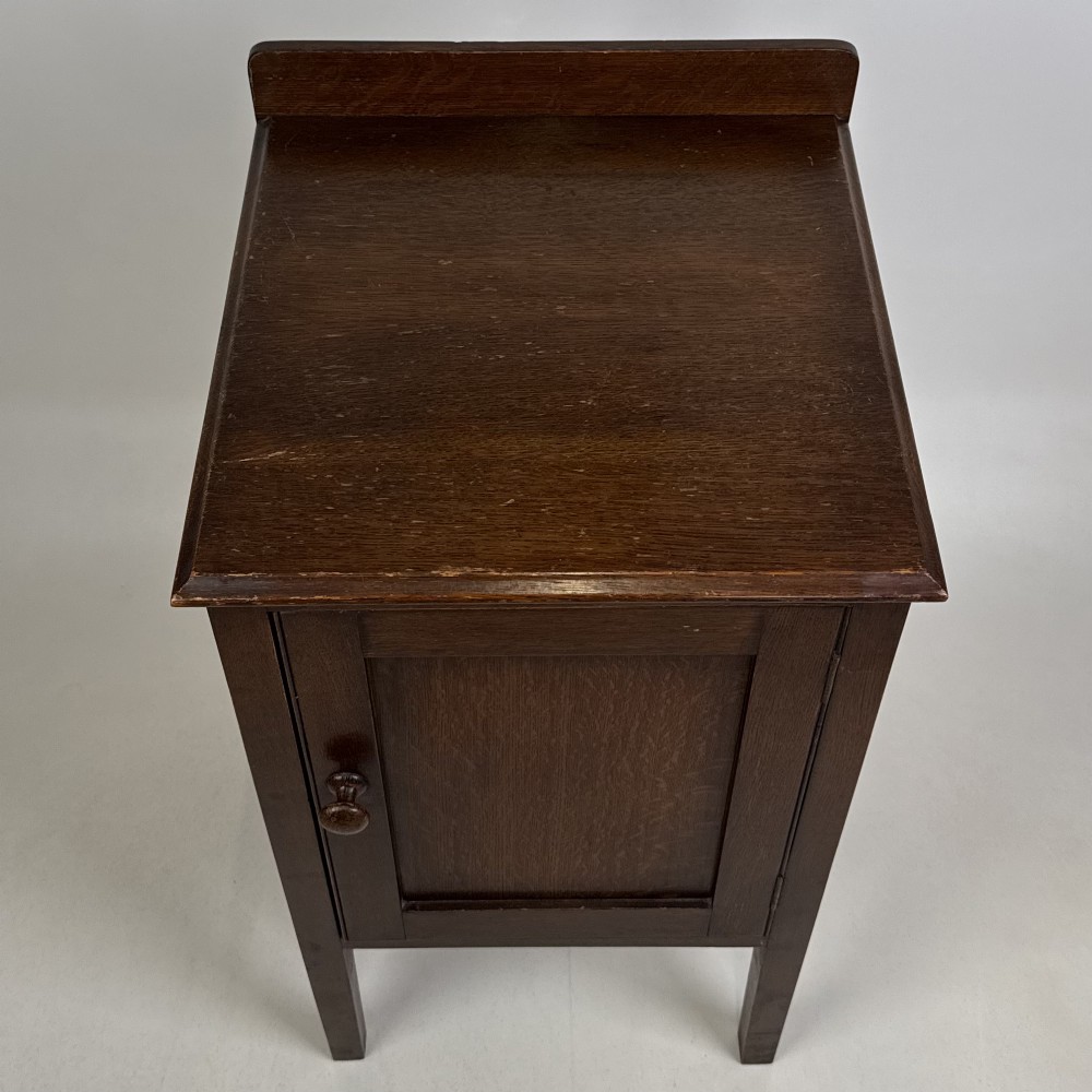 An Edwardian dark brown oak cabinet featuring a single panelled door with a round wooden knob supported on four square straight legs. View X