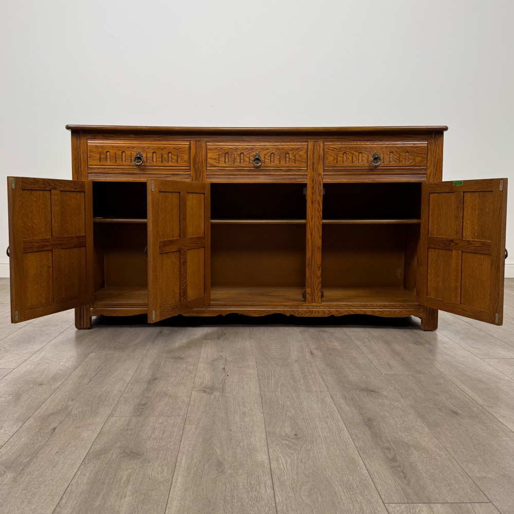 A three-door golden oak sideboard featuring three carved drawers, panelled cabinet doors, and metal drop handles. View II