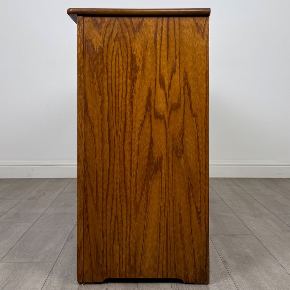 A three-door golden oak sideboard featuring three carved drawers, panelled cabinet doors, and metal drop handles. View IV