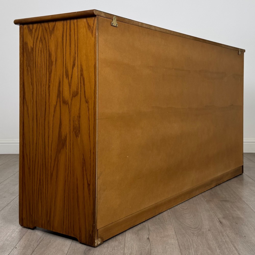 A three-door golden oak sideboard featuring three carved drawers, panelled cabinet doors, and metal drop handles. View V