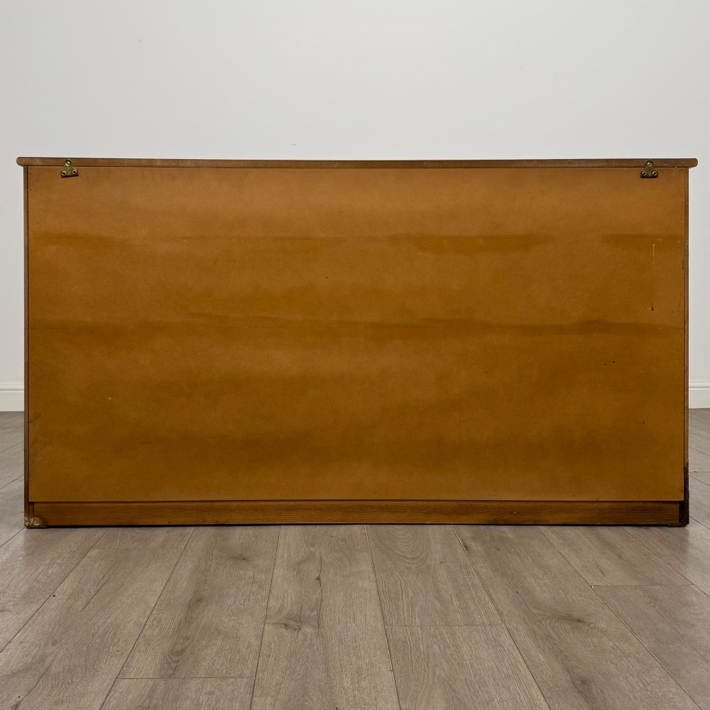 A three-door golden oak sideboard featuring three carved drawers, panelled cabinet doors, and metal drop handles. View VI