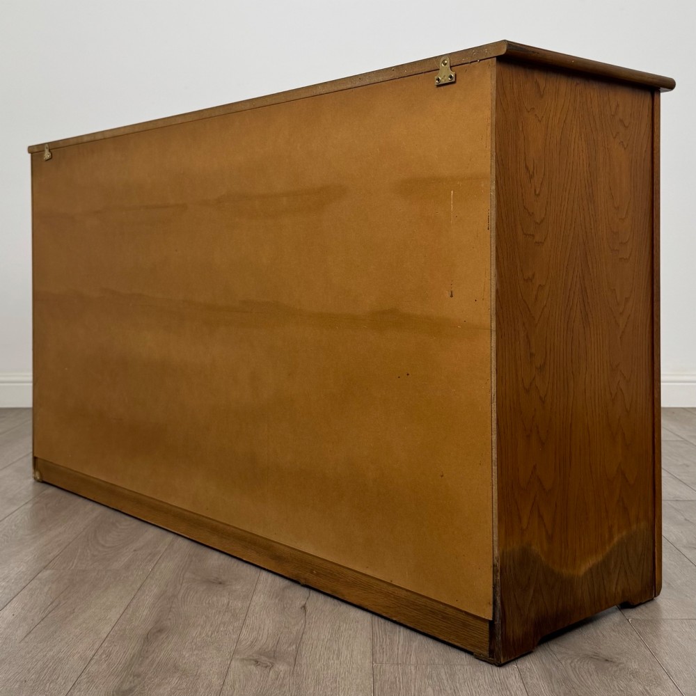 A three-door golden oak sideboard featuring three carved drawers, panelled cabinet doors, and metal drop handles. View VII