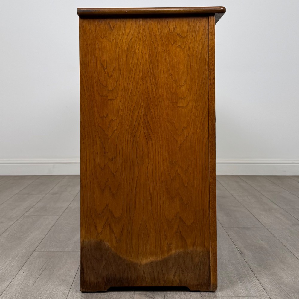 A three-door golden oak sideboard featuring three carved drawers, panelled cabinet doors, and metal drop handles. View VIII