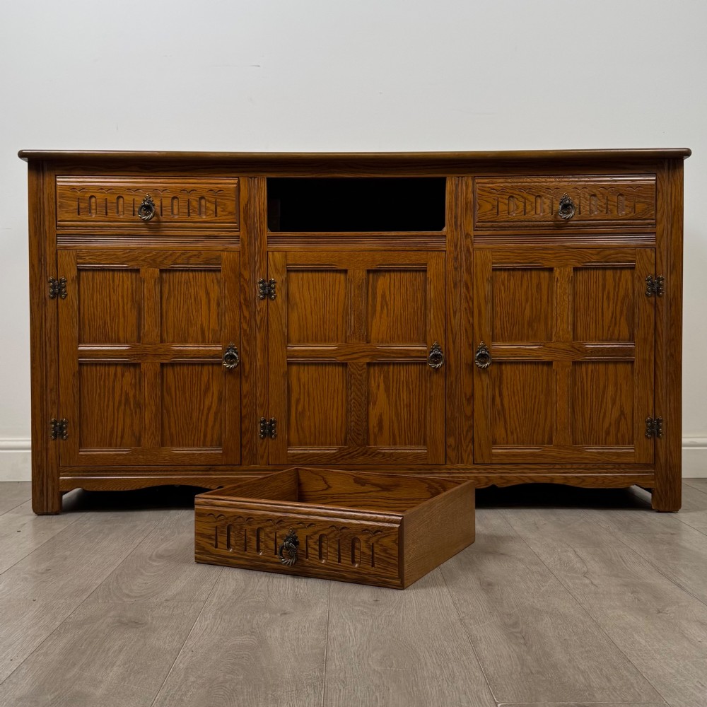 A three-door golden oak sideboard featuring three carved drawers, panelled cabinet doors, and metal drop handles. View XI