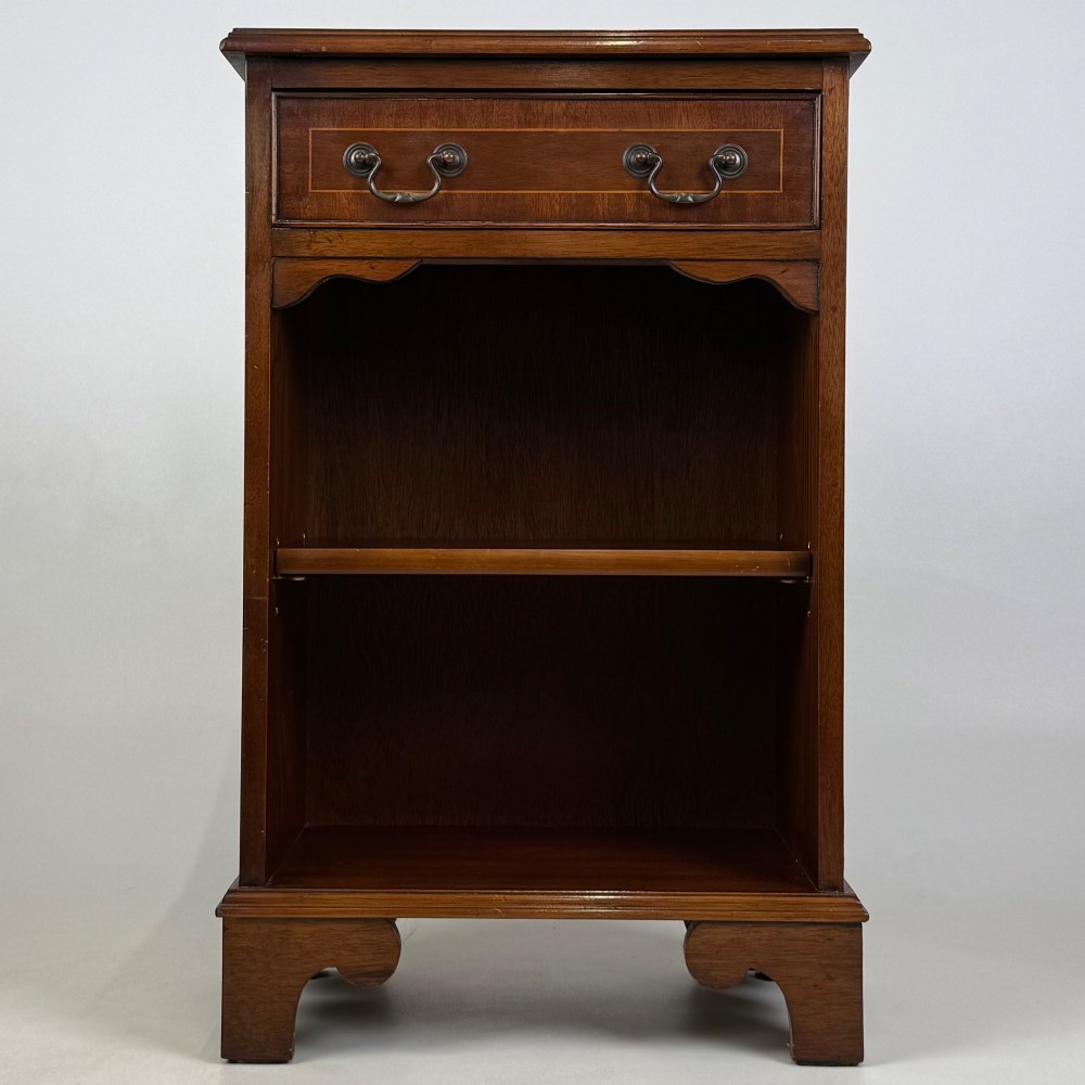 A small mahogany open bookcase featuring a single top drawer with brass swan-neck handles, satinwood inlay, open lower shelving, and shaped bracket feet.