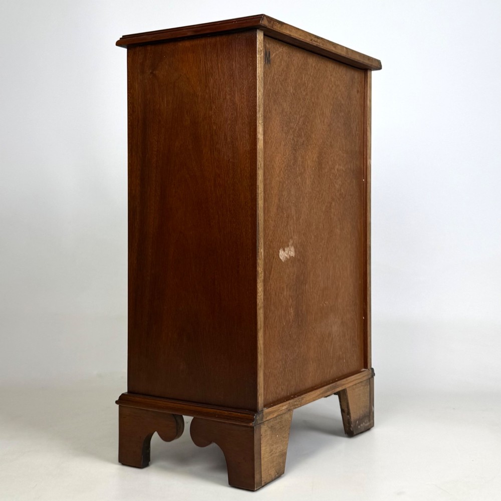 A small mahogany open bookcase featuring a single top drawer with brass swan-neck handles, satinwood inlay, open lower shelving, and shaped bracket feet. View IV