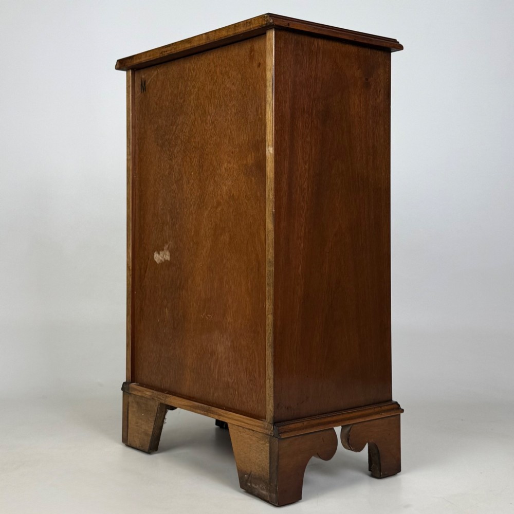 A small mahogany open bookcase featuring a single top drawer with brass swan-neck handles, satinwood inlay, open lower shelving, and shaped bracket feet. View VI