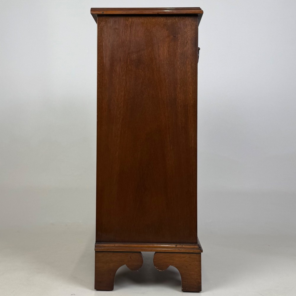 A small mahogany open bookcase featuring a single top drawer with brass swan-neck handles, satinwood inlay, open lower shelving, and shaped bracket feet. View VII