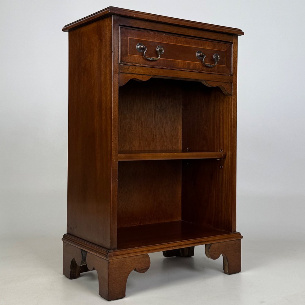A small mahogany open bookcase featuring a single top drawer with brass swan-neck handles, satinwood inlay, open lower shelving, and shaped bracket feet. View VIII