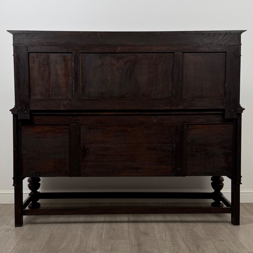 A dark oak Jacobean style sideboard featuring a raised upper superstructure, geometric carved panelling, drawers with brass drop handles, and turned bulbous legs connected by a stretcher base. View VI