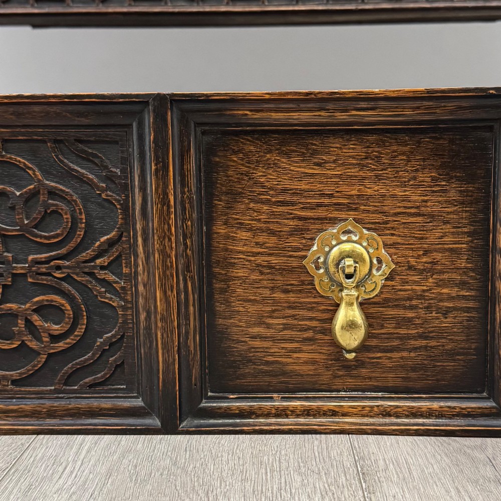 A dark oak Jacobean style sideboard featuring a raised upper superstructure, geometric carved panelling, drawers with brass drop handles, and turned bulbous legs connected by a stretcher base. View XII
