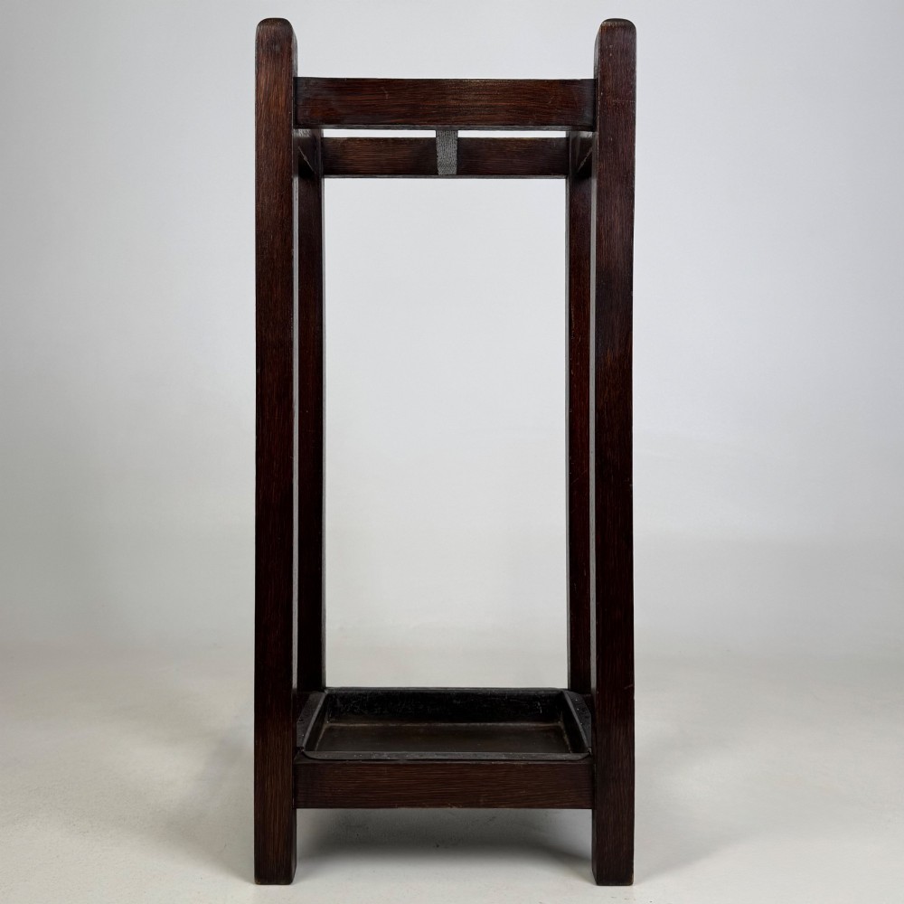 A small dark oak Edwardian umbrella stand featuring a square wooden frame with an upper section divider and a metal drip tray at the base.