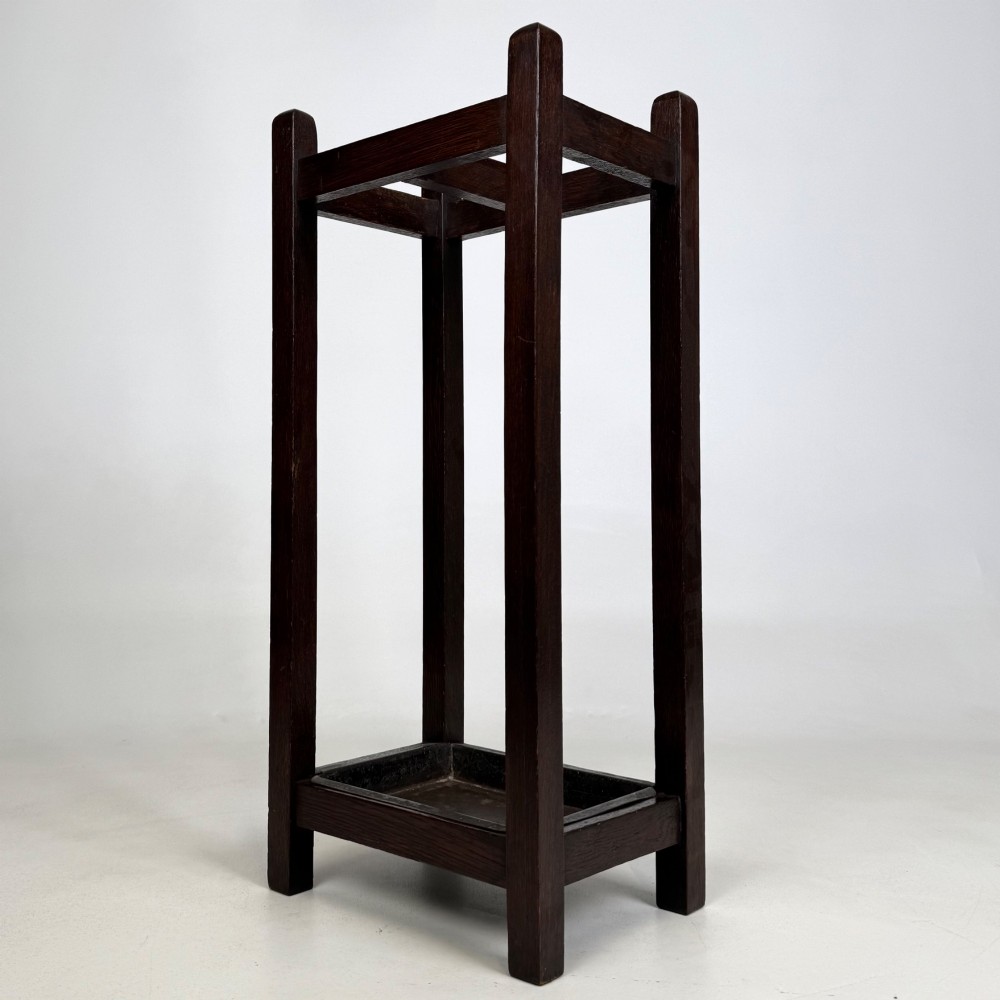 A small dark oak Edwardian umbrella stand featuring a square wooden frame with an upper section divider and a metal drip tray at the base. View VI