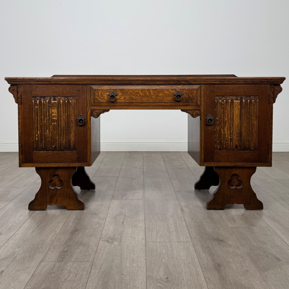 A 20th-century carved oak pedestal desk featuring linenfold cupboard doors, a central top drawer, and trefoil pierced end supports.