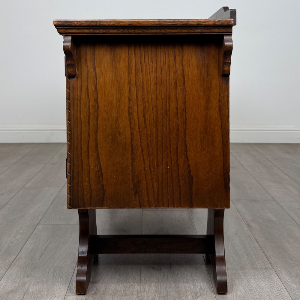 A 20th-century carved oak pedestal desk featuring linenfold cupboard doors, a central top drawer, and trefoil pierced end supports. View IV