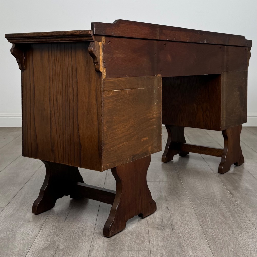 A 20th-century carved oak pedestal desk featuring linenfold cupboard doors, a central top drawer, and trefoil pierced end supports. View V