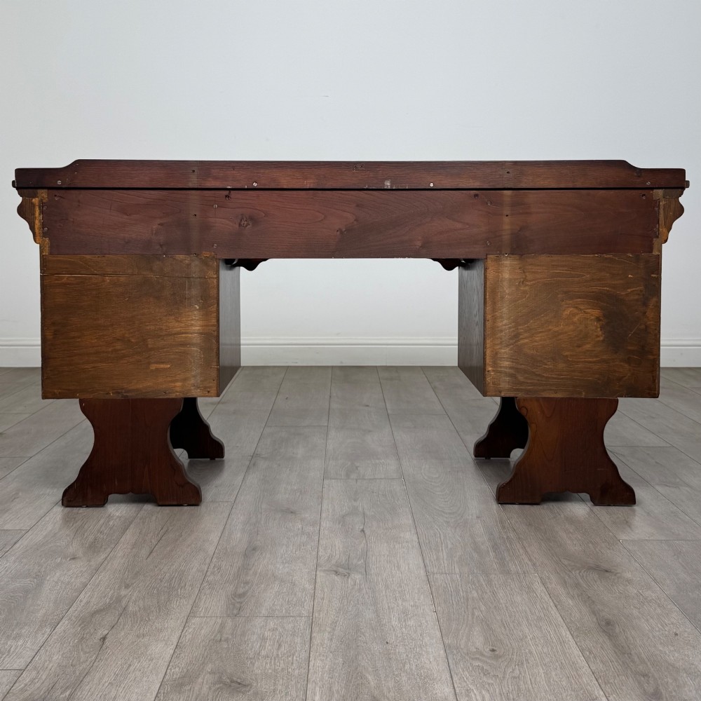A 20th-century carved oak pedestal desk featuring linenfold cupboard doors, a central top drawer, and trefoil pierced end supports. View VI