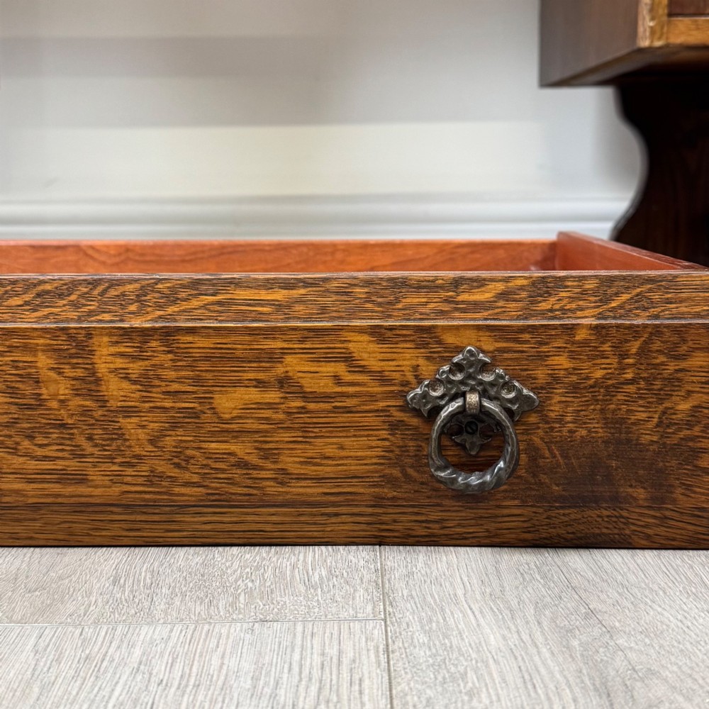 A 20th-century carved oak pedestal desk featuring linenfold cupboard doors, a central top drawer, and trefoil pierced end supports. View XII