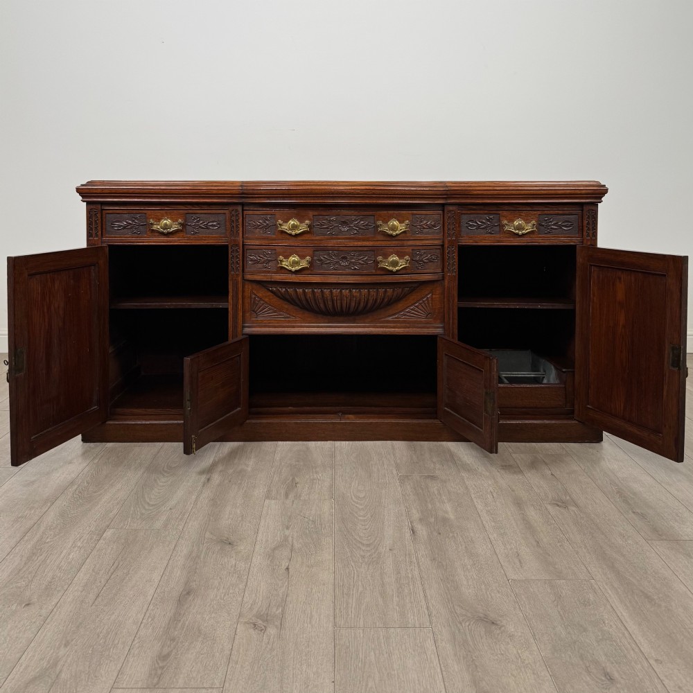 A wide 19th-century Victorian dark oak sideboard featuring relief-carved floral panels, central drawers with brass handles, and lower cupboard doors. View II