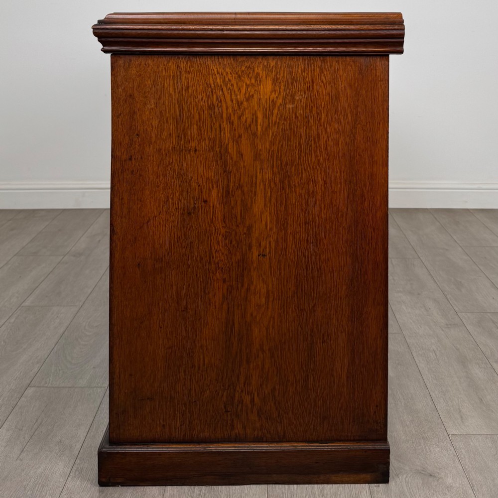 A wide 19th-century Victorian dark oak sideboard featuring relief-carved floral panels, central drawers with brass handles, and lower cupboard doors. View IV