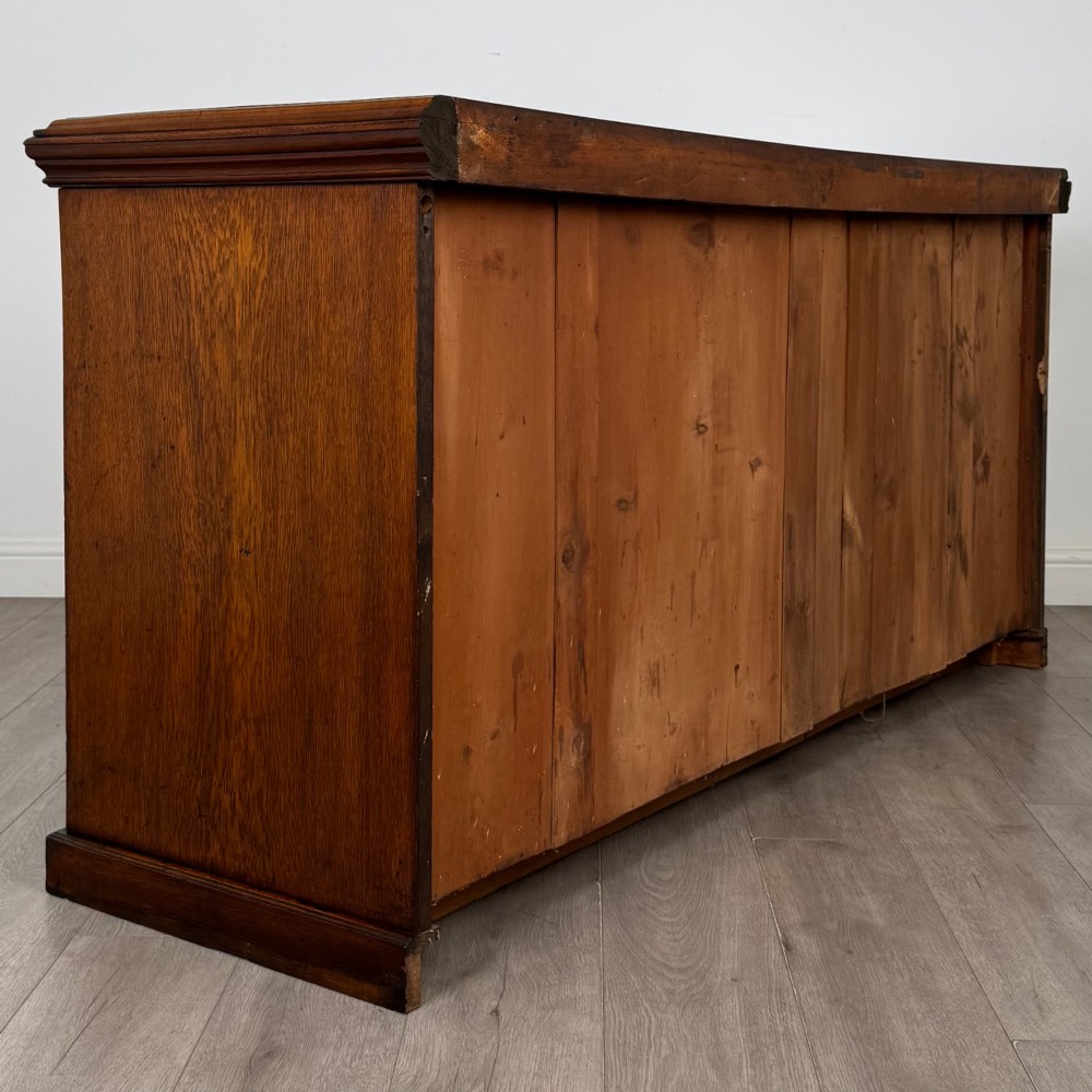 A wide 19th-century Victorian dark oak sideboard featuring relief-carved floral panels, central drawers with brass handles, and lower cupboard doors. View V