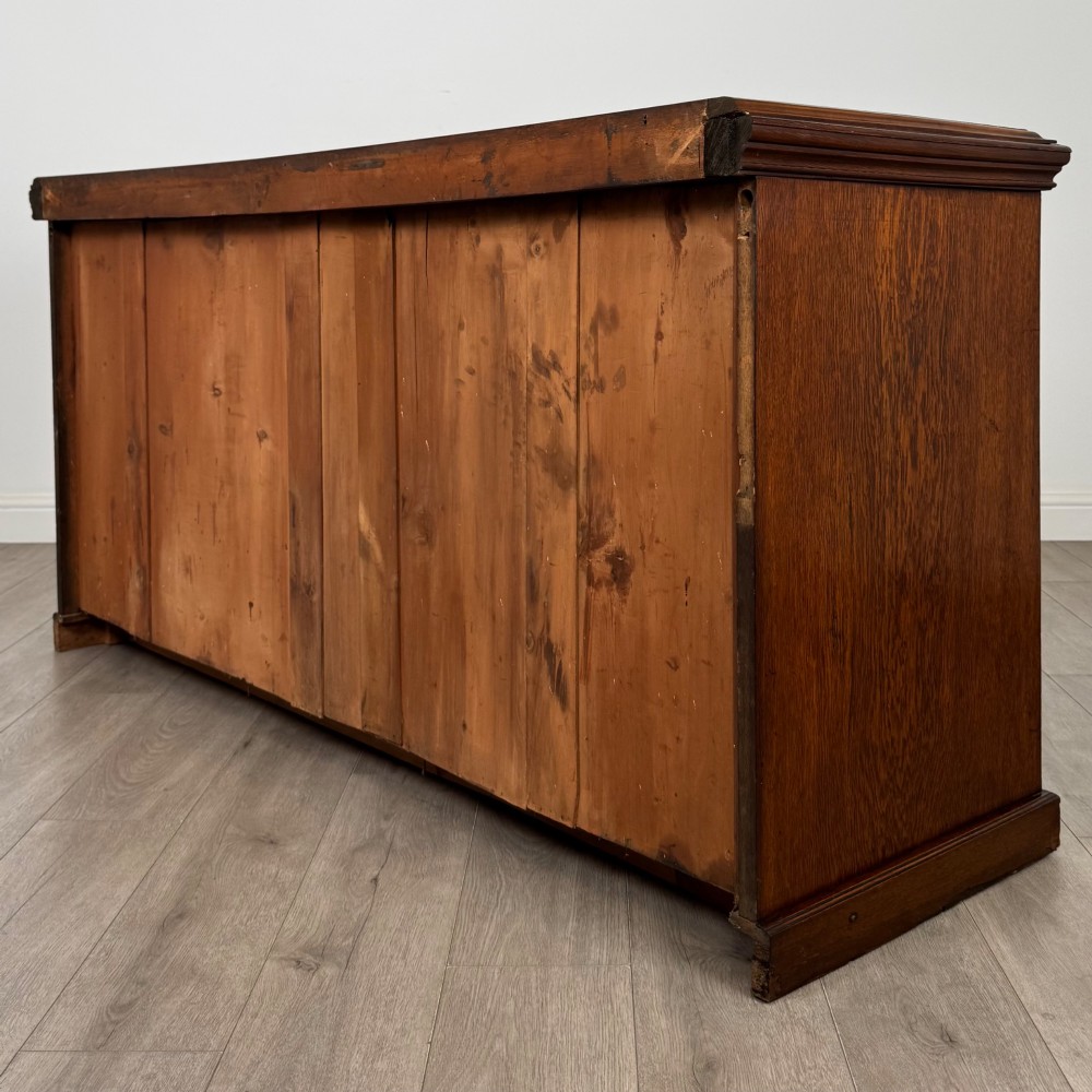 A wide 19th-century Victorian dark oak sideboard featuring relief-carved floral panels, central drawers with brass handles, and lower cupboard doors. View VII