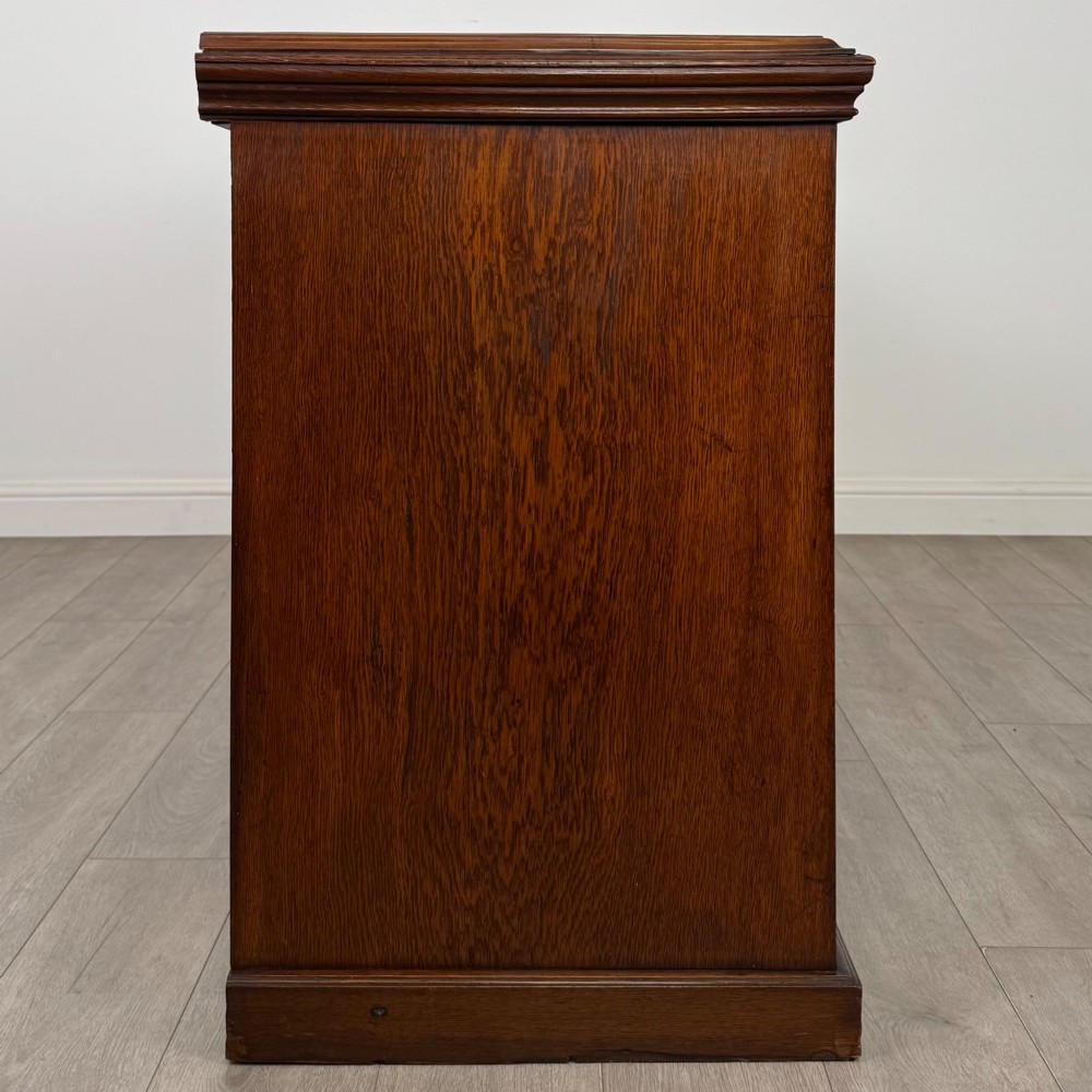 A wide 19th-century Victorian dark oak sideboard featuring relief-carved floral panels, central drawers with brass handles, and lower cupboard doors. View VIII
