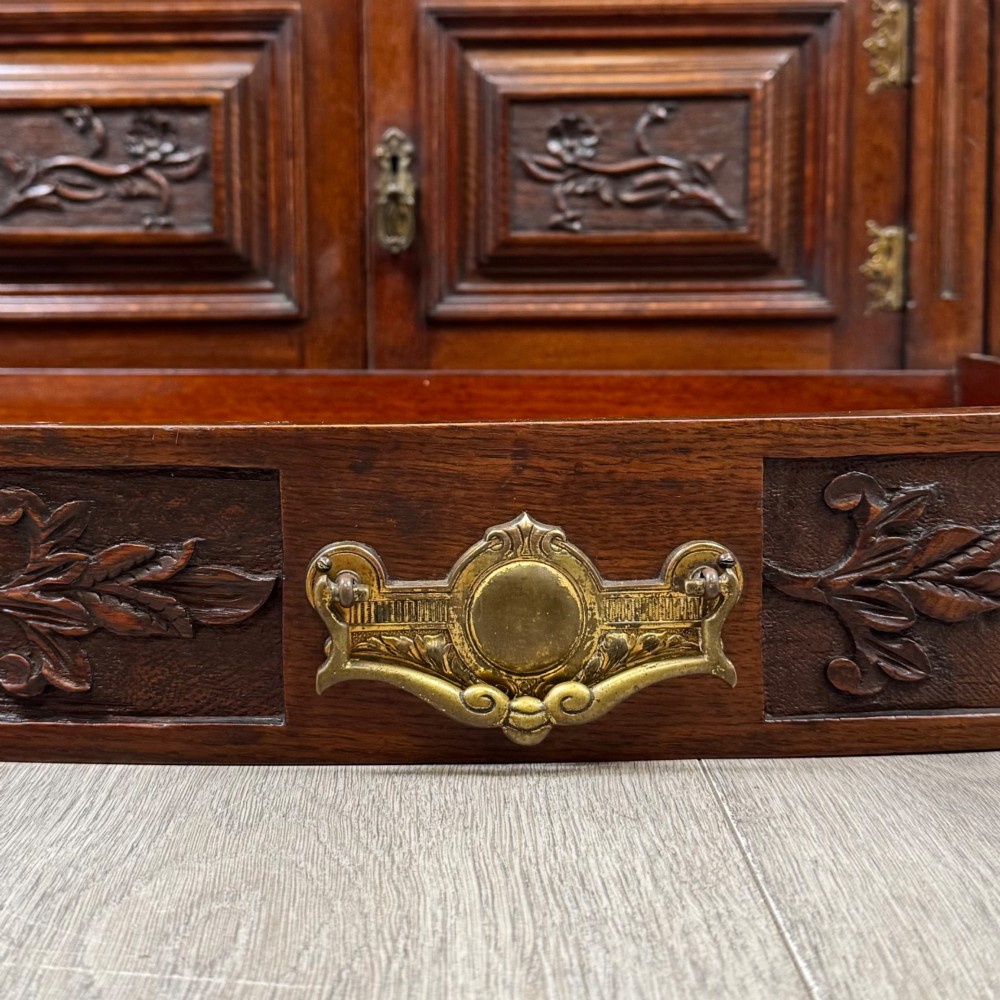 A wide 19th-century Victorian dark oak sideboard featuring relief-carved floral panels, central drawers with brass handles, and lower cupboard doors. View XII