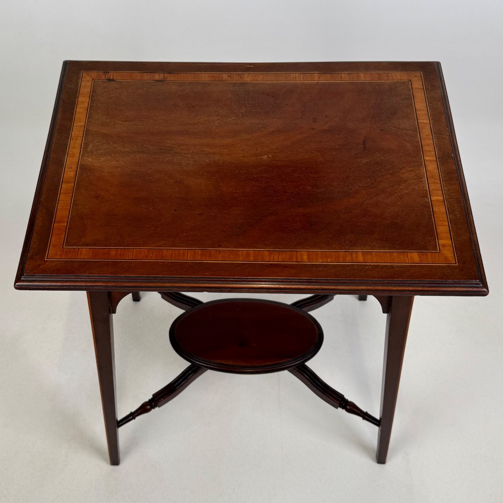 An Edwardian mahogany side table featuring a square top, splayed legs, corner spandrels, and a central circular undertier supported by shaped stretchers. View IX