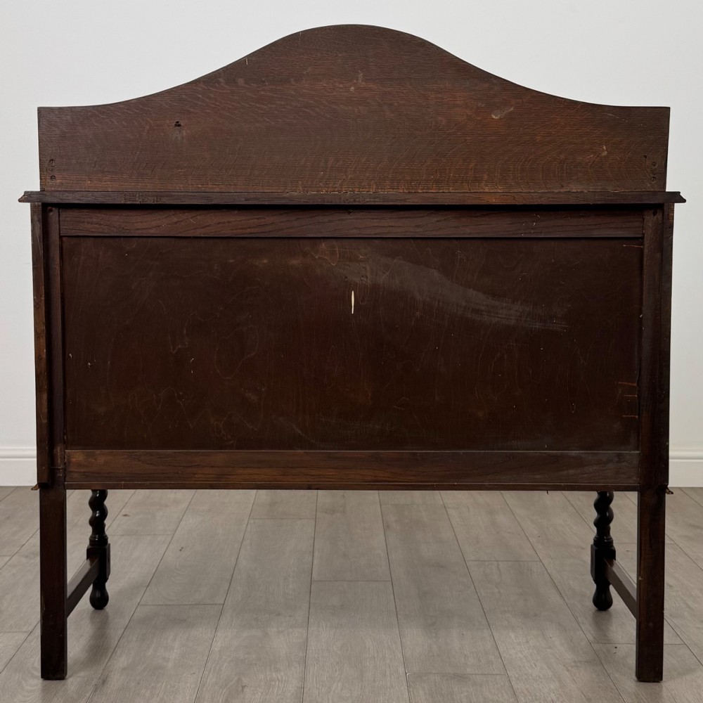 An Edwardian dark oak sideboard featuring a shaped upstand gallery, two top drawers with brass drop handles, twin raised-panel cupboard doors, and front barley twist legs. View VI