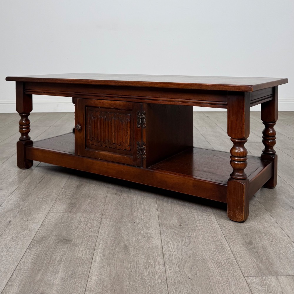 A low rectangular warm brown oak coffee table featuring turned baluster legs, a lower shelf, and a central cupboard door decorated with carved linenfold panelling. View III